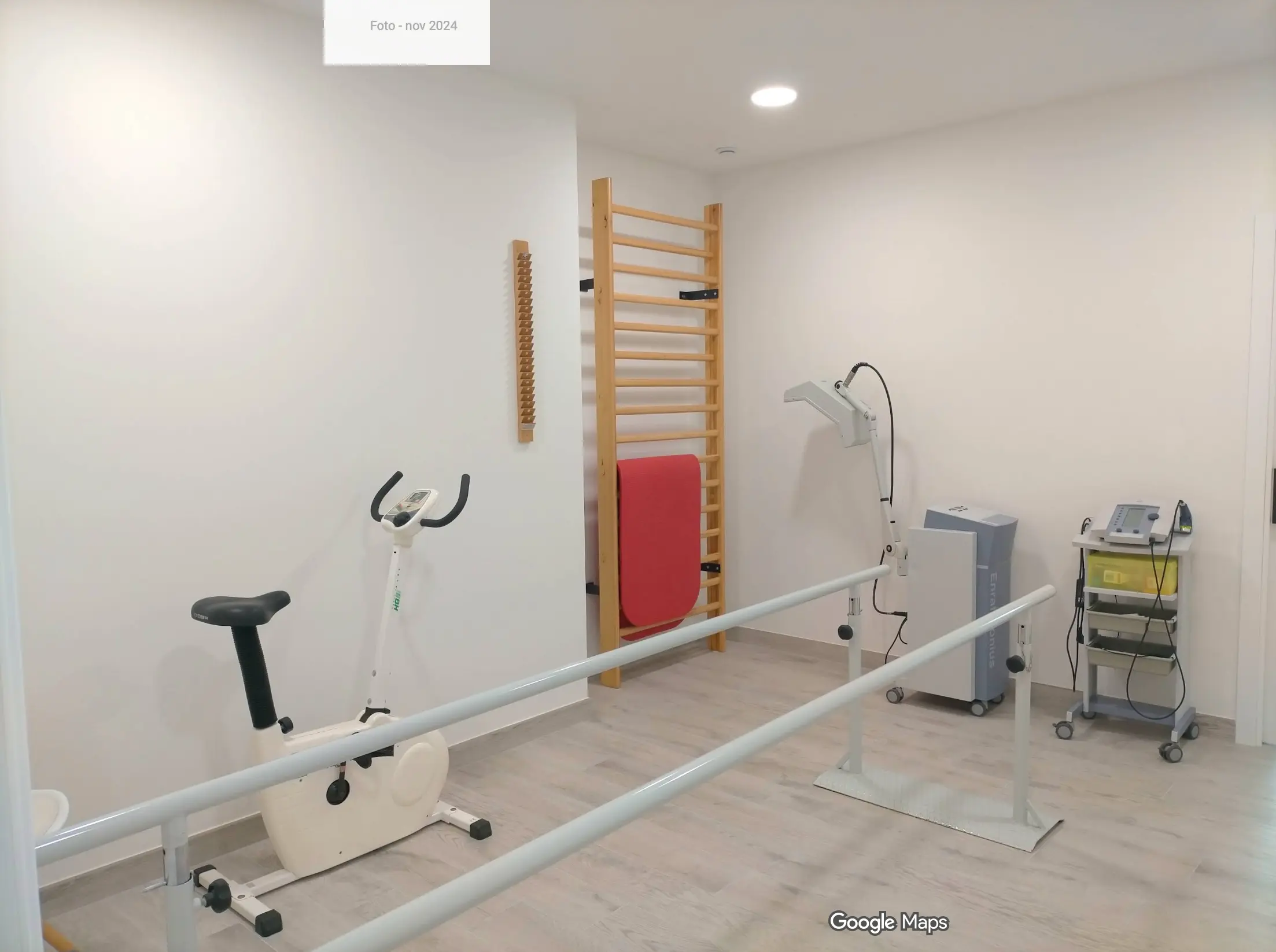 Gimnasio de rehabilitación con barras paralelas, bicicleta estática, espaldera de madera y equipos de electroterapia
